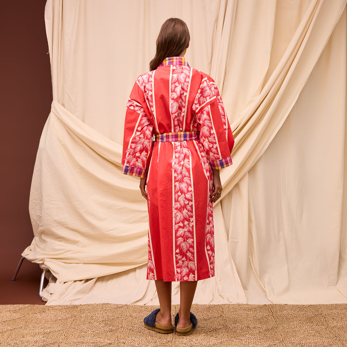 Person wearing a red floral robe standing in front of beige curtains.
