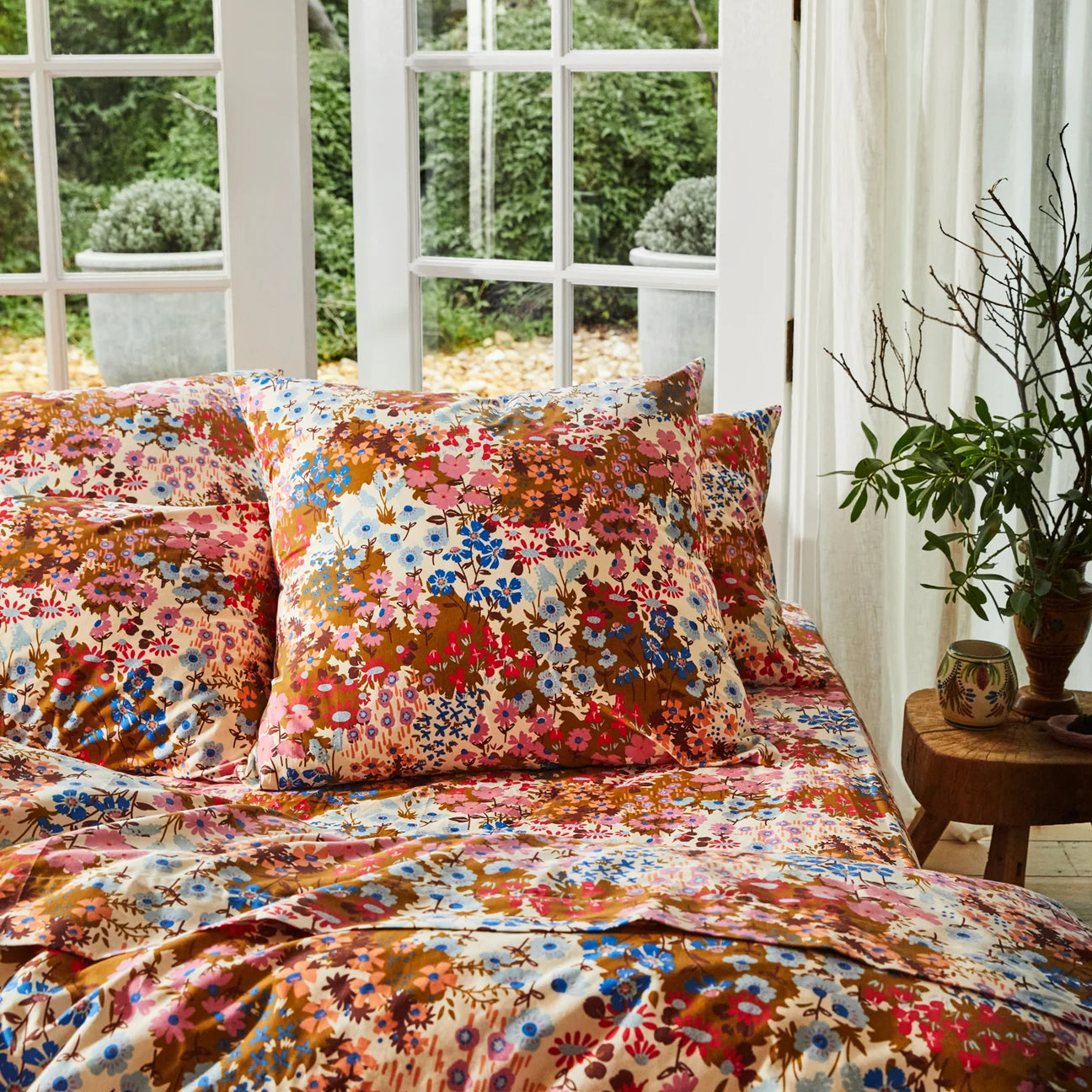 Floral bedding set on a bed in a room with plants and garden view.