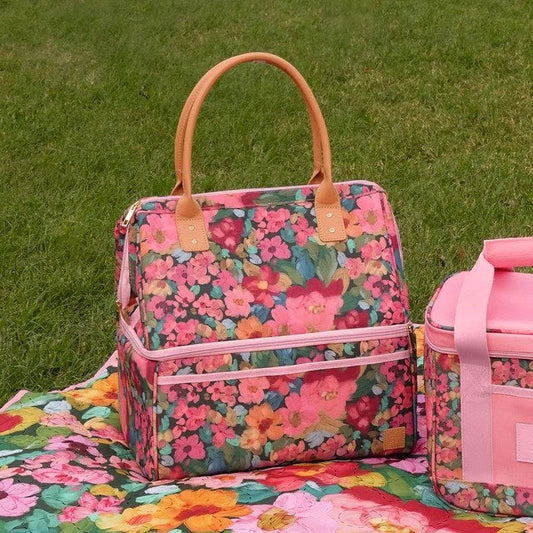A pink floral insulated tote bag with tan handles sits on a grassy lawn next to a matching pink floral lunch bag.