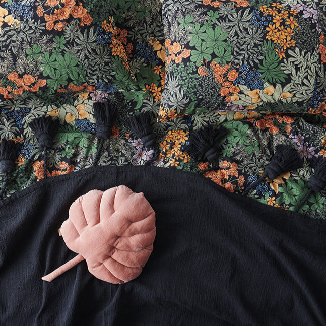 Floral and greenery patterned fabric with a black blanket and pink plant shaped cushion.
