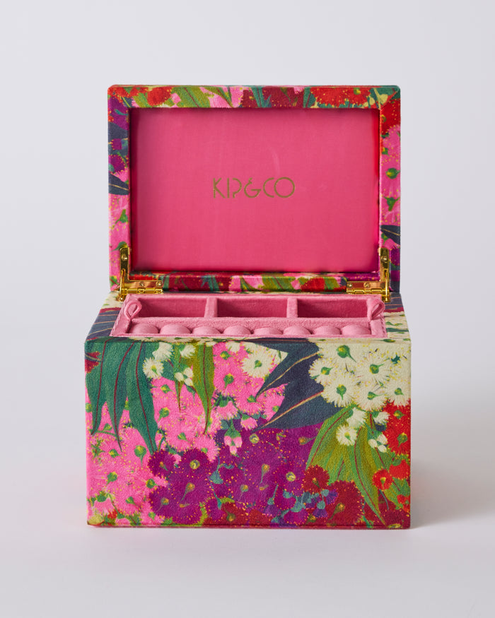 An open jewelry box with a vibrant floral print exterior and a solid pink interior. The brand name 'KIP&CO' is printed in gold on the pink inner lid.