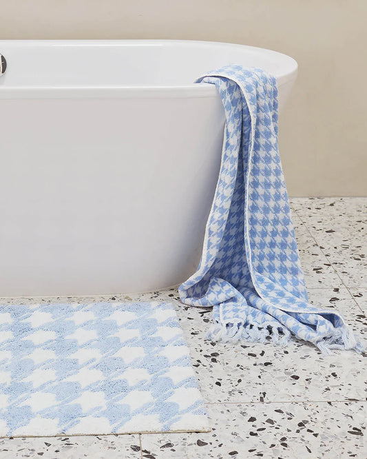Blue and white patterned towel draped over a white bathtub on a terrazzo floor. Matching bath mat on floor in front of bath tub, blue and white pattern.