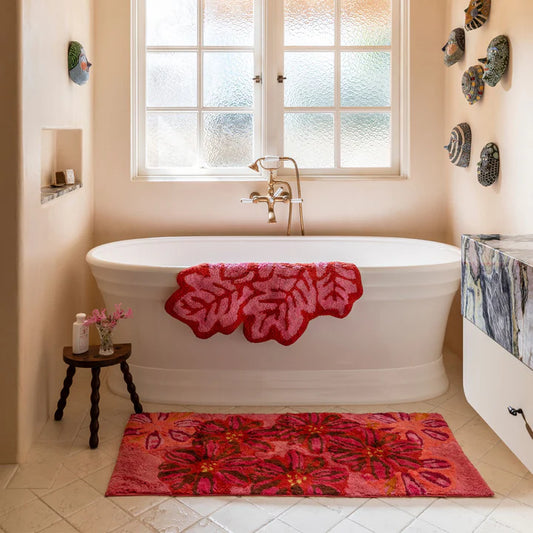 Bathroom with a freestanding bathtub and pink floral bath mats. Featuring product listed, hanging over edge of bath tub pink and red leaf pattern bath mat in cut out shape of leafs.