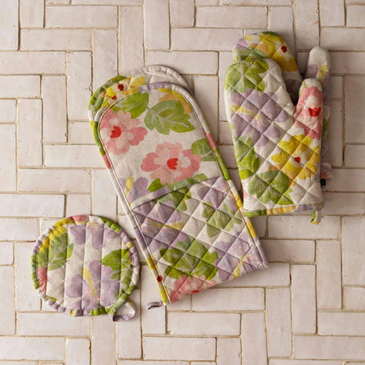 Tiled background with oven mitt pair, long oven mitt and small round linen oven mitt, all in same aloha floral print. Natural linen base with green, pink, lilac and yellow flowers.