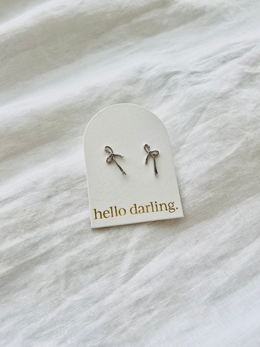 Pair of bow-shaped earrings on a 'hello darling' card against a white fabric background. Available at Hello Darling, Albury Wodonga Beechworth and Bright.