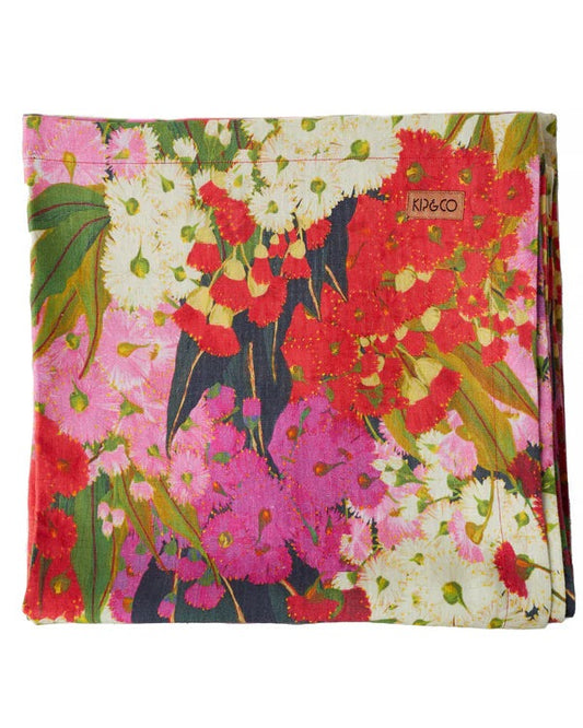 A linen tablecloth with a floral pattern featuring rich pinks, reds, and creamy white colors, laid flat.