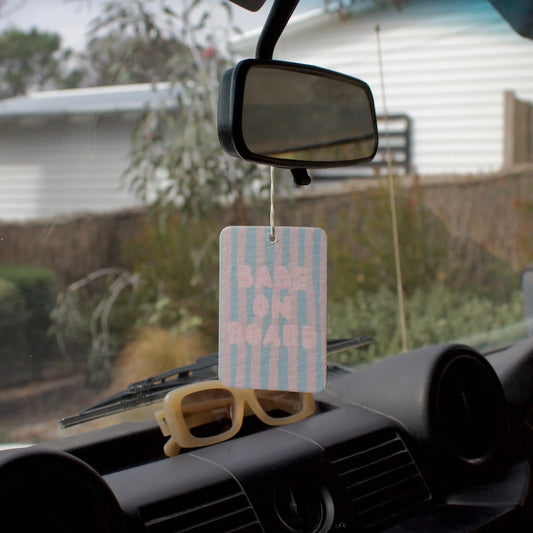 Car dashboard with sunglasses and a striped air freshener hanging from the rearview mirror.