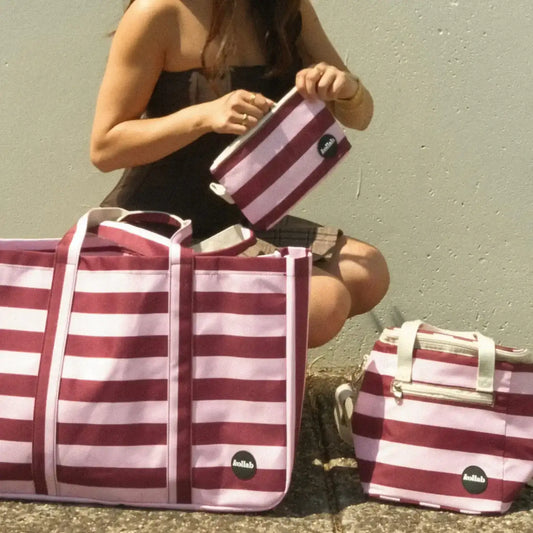 Person holding a red and white striped bag with two smaller bags on a concrete surface.