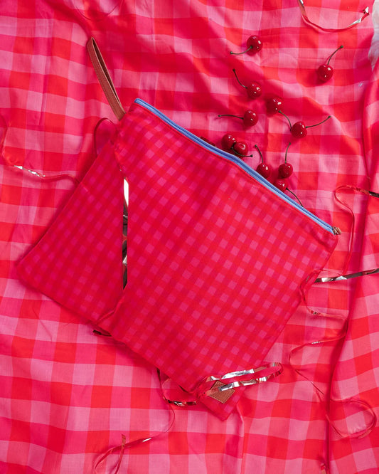 Red checkered bag with blue zipper on a red and white checkered background with cherries.