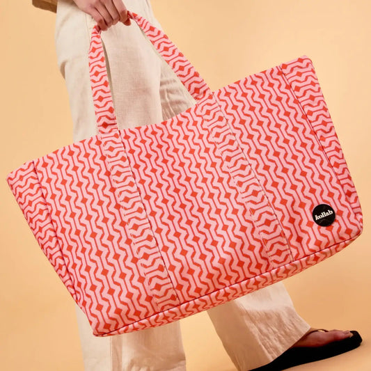Person holding a pink patterned bag with a visible brand logo on a beige background