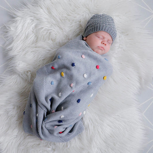 Newborn baby wrapped in a gray polka dot blanket on a white fluffy surface
