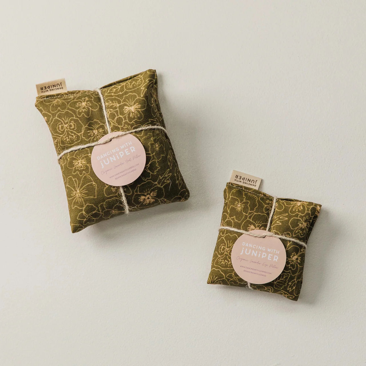 Green fabric heat pillow and eye pillow with pink labels on a light gray background.