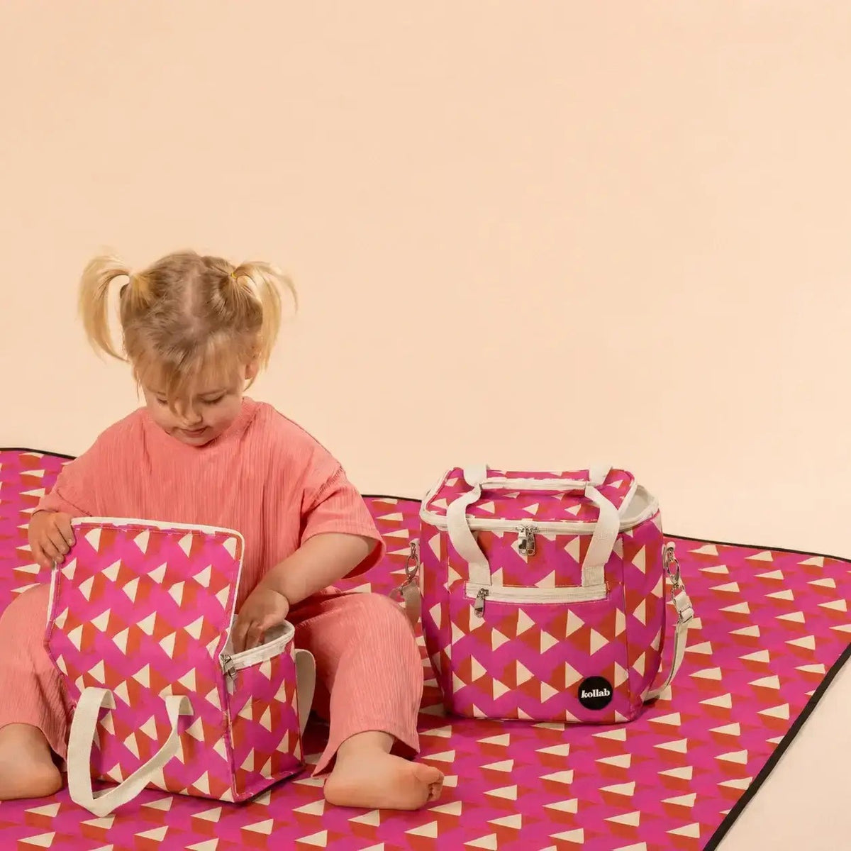Child sits on picnic mat with mini cooler and lunch box in same print sat next to child.