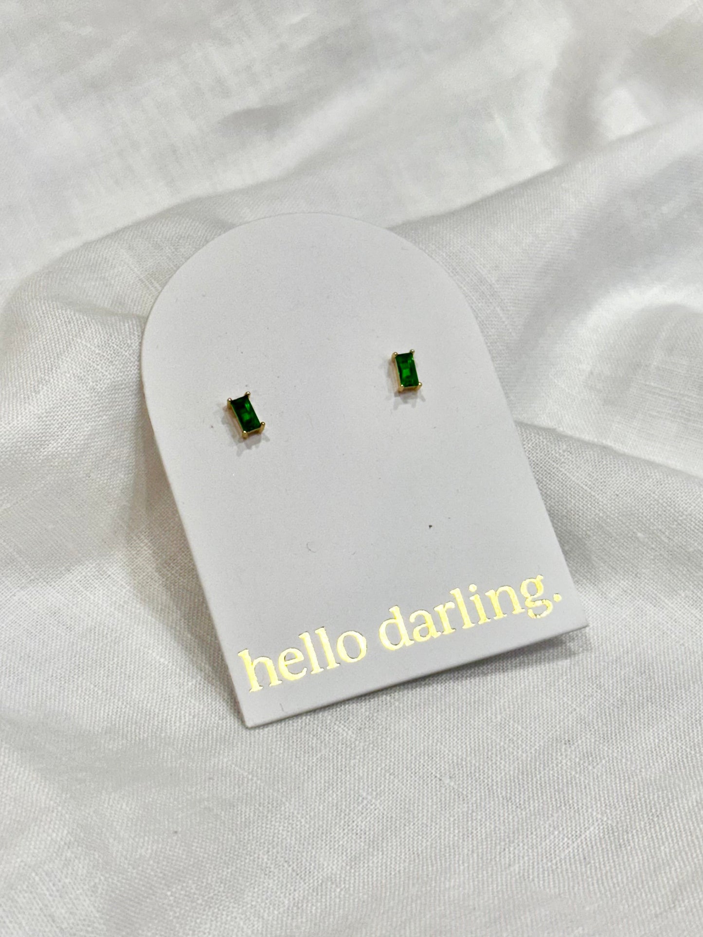 Green gemstone earrings on a 'hello darling' card against a white fabric background
