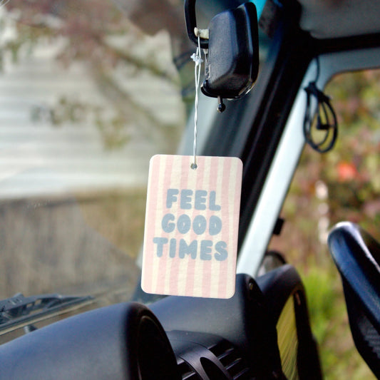 Car air freshener with 'FEEL GOOD TIMES' text hanging from a car's rearview mirror.