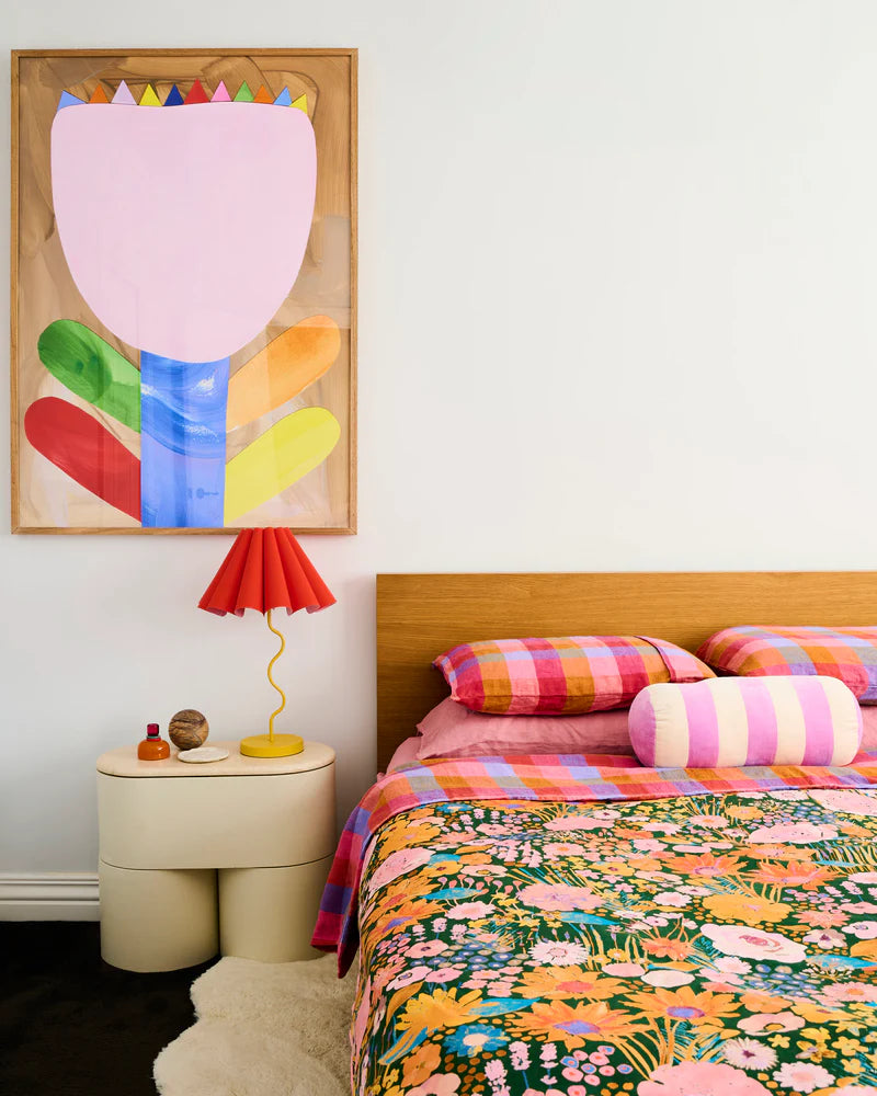 Bedroom with colorful artwork and bedding, and a lamp on a nightstand.