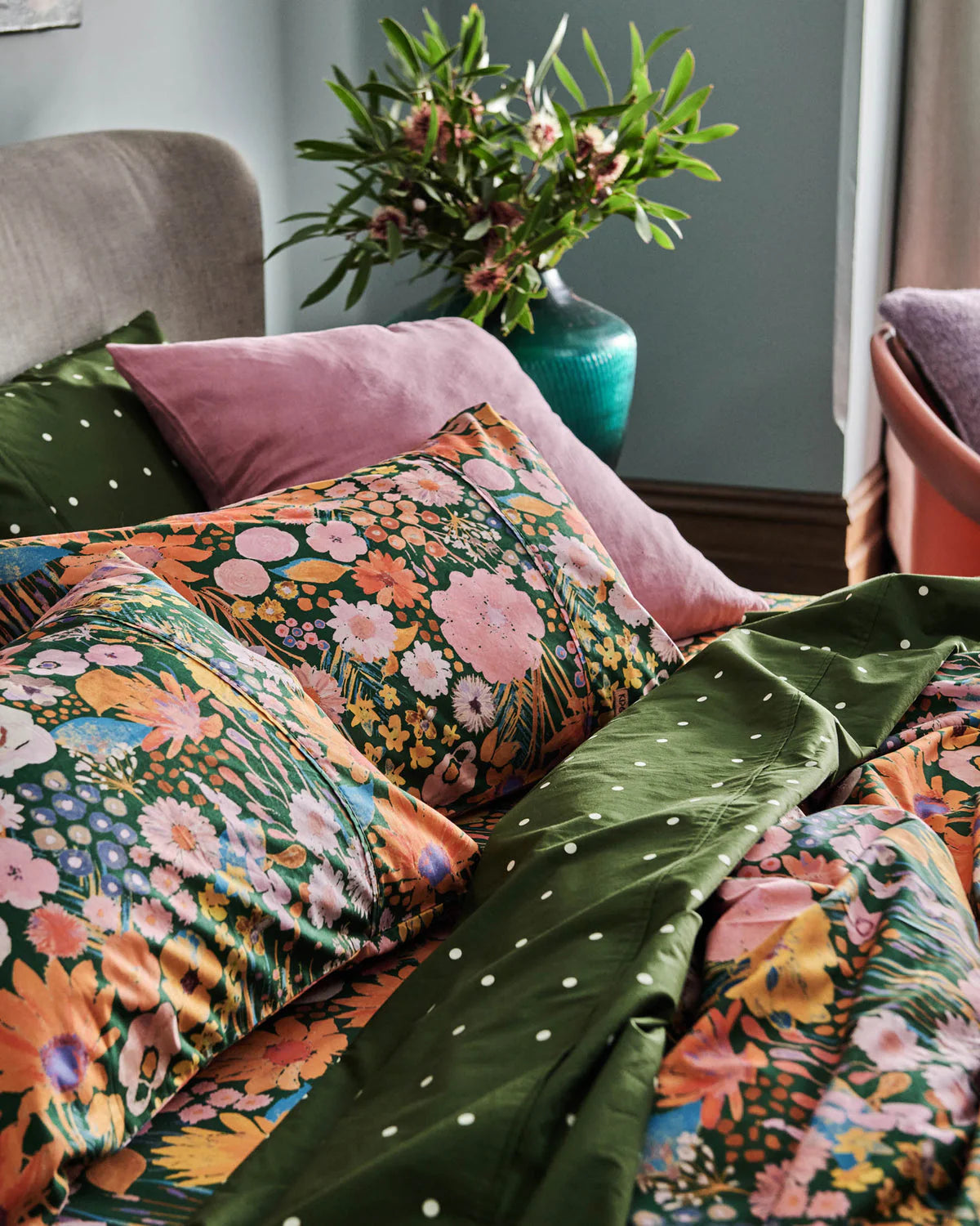 Floral and green patterned bedding with a vase of flowers in the background.