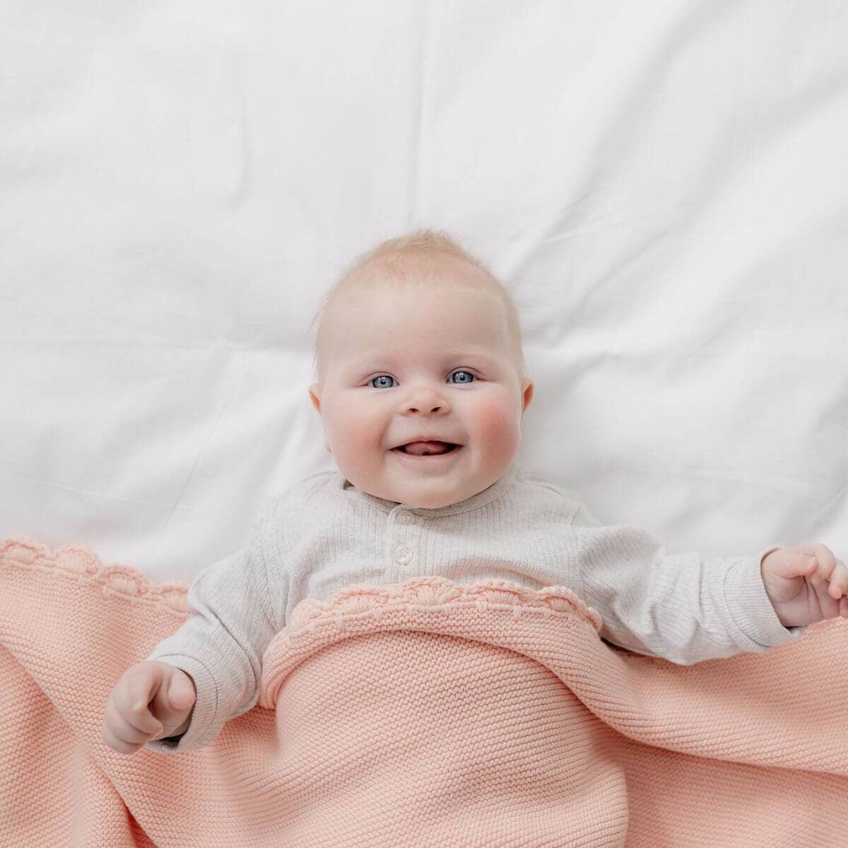Baby lying on a white blanket with a pink blanket underneath