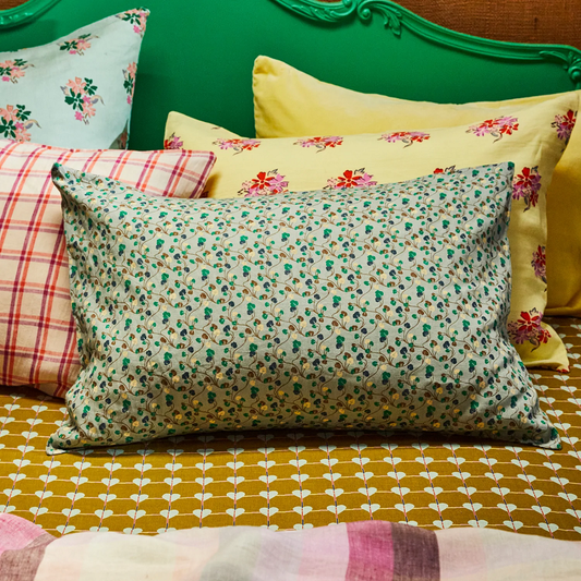 Colorful pillows with floral and plaid patterns on a bed with a green headboard.