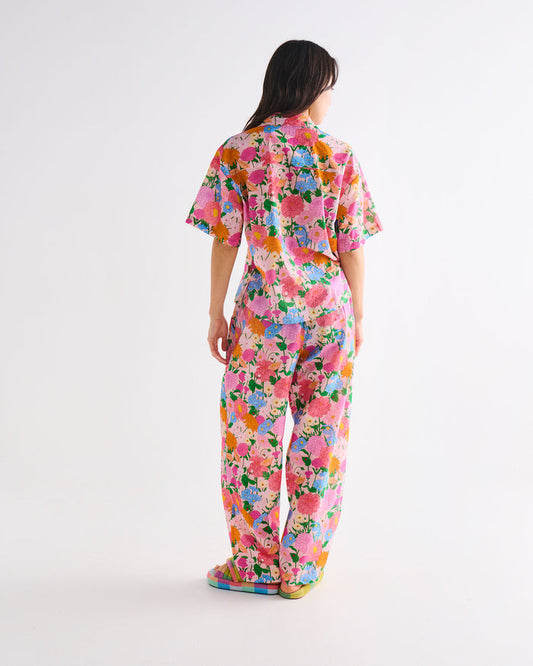 A model viewed from behind wearing a short-sleeve, wide-leg floral jumpsuit with a vibrant multicolor print on a solid white studio background.