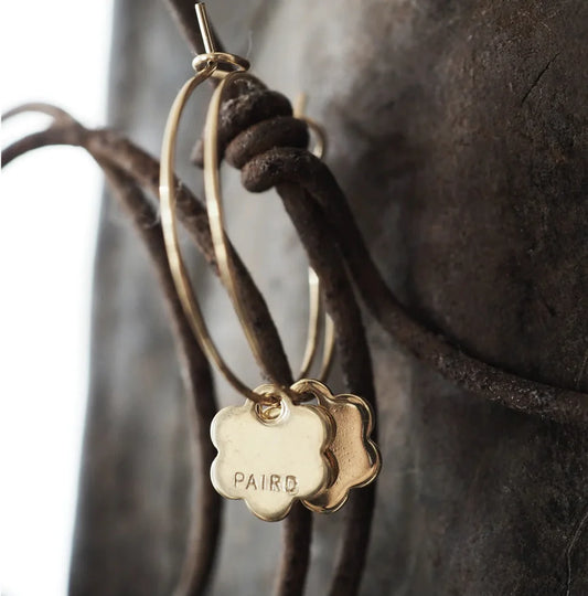 Gold hoop earrings with a flower-shaped pendant on a textured surface.
