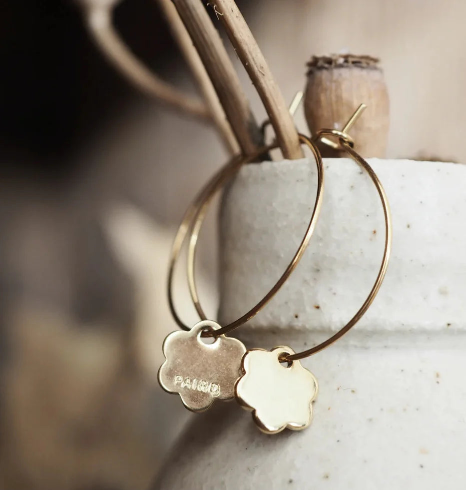 Gold hoop earrings with floral charm on a textured surface