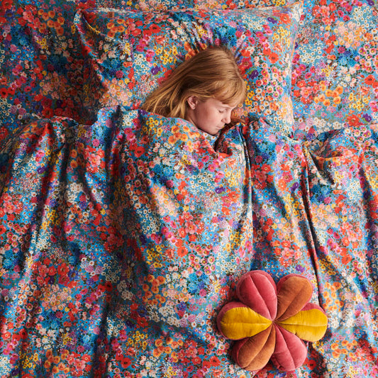 Child sleeping under a colorful floral blanket with a pillow nearby.