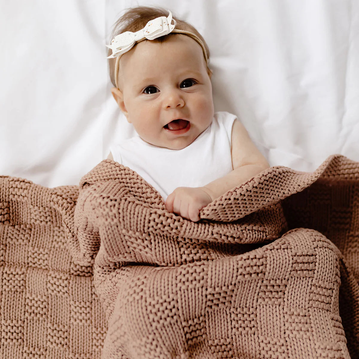 Baby wrapped in a brown blanket with a white headband on a white background