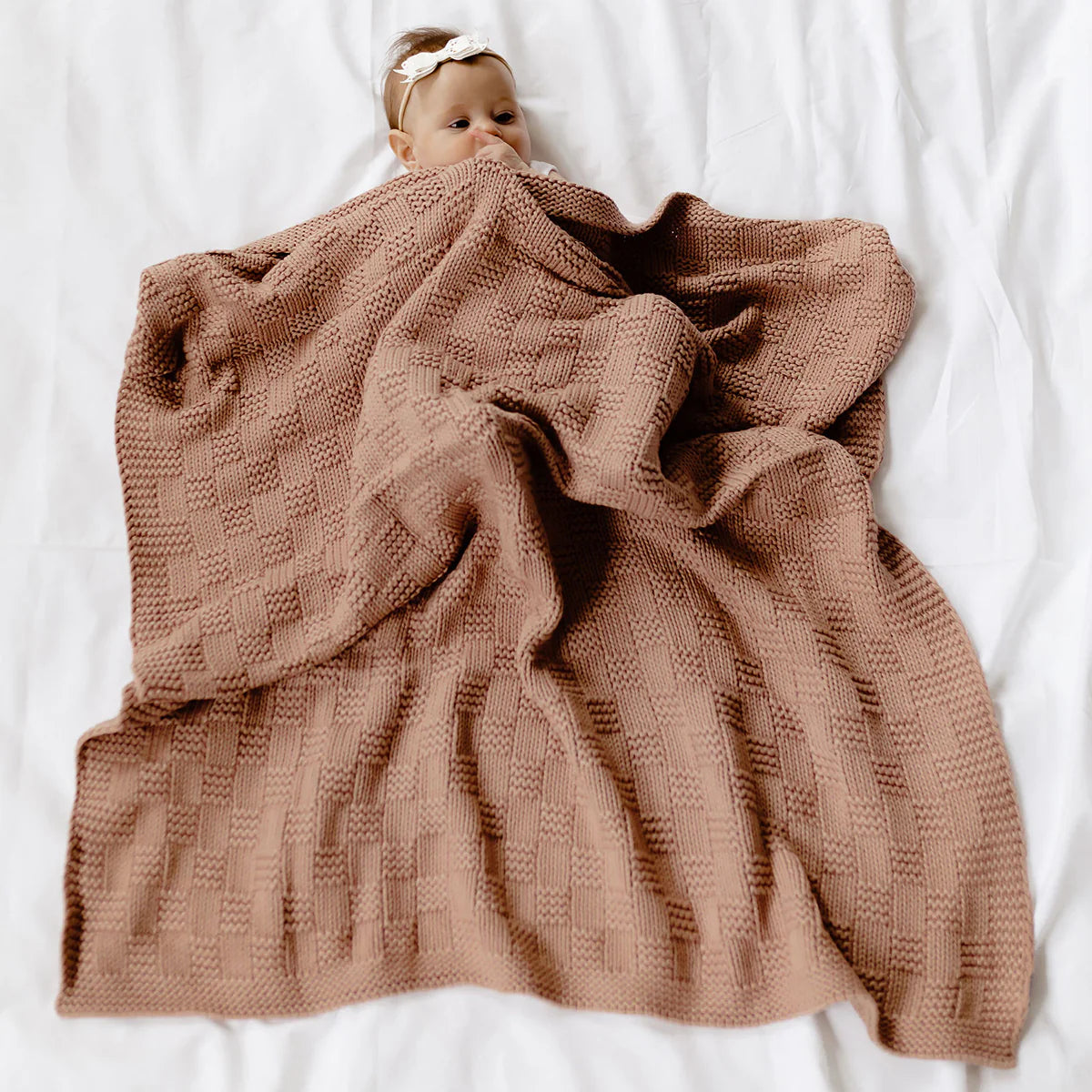 Baby wrapped in a brown textured blanket on a white surface
