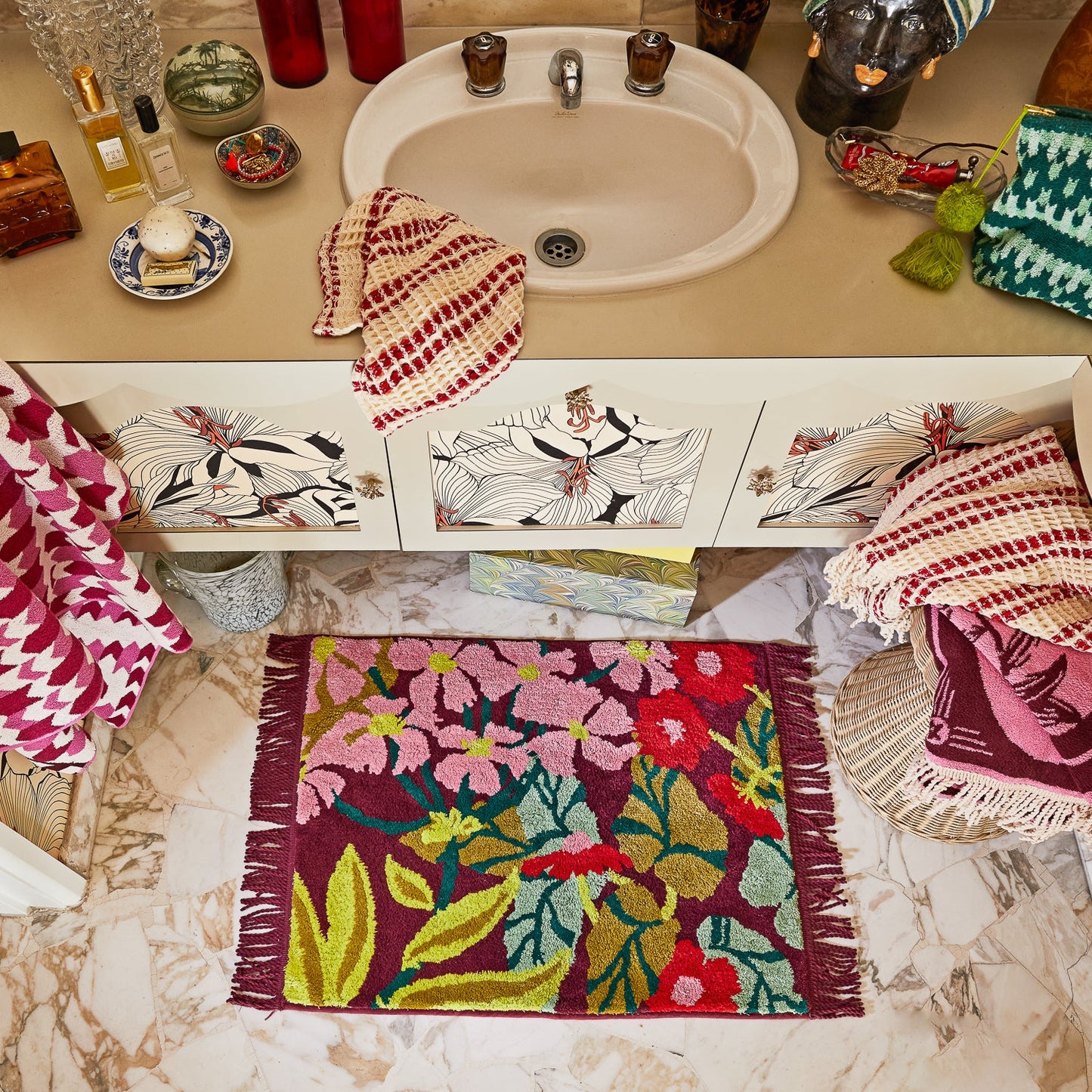 Colorful bath mat with floral pattern on a bathroom floor, with sink and towels in the background.