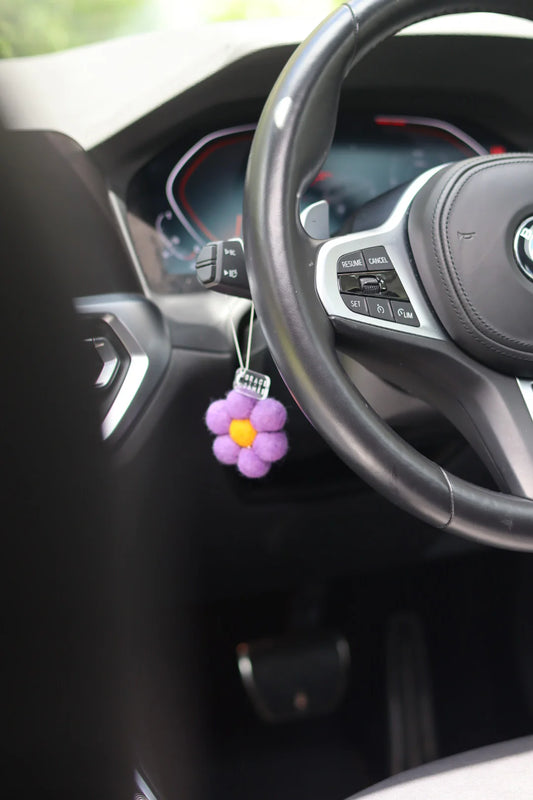 Purple flower-shaped car air freshener hanging from a car dashboard.