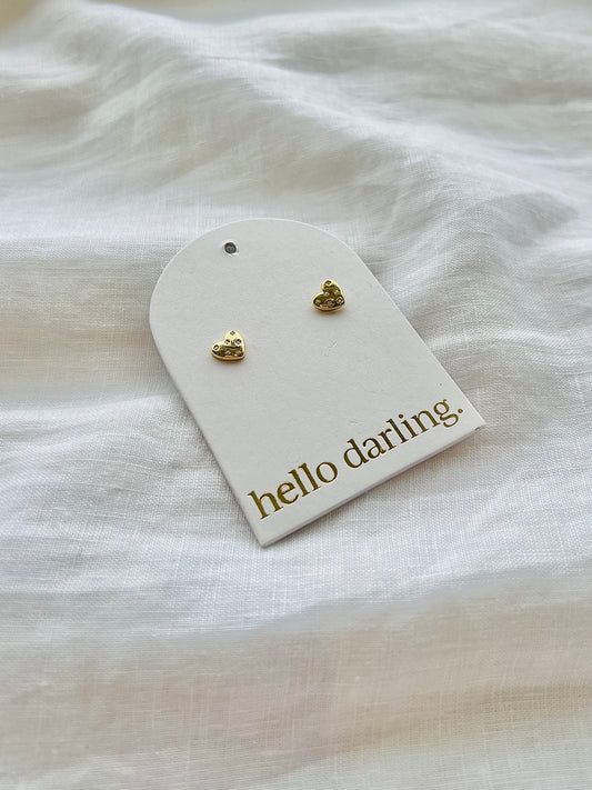 Gold heart-shaped earrings on a 'hello darling' card against a white fabric background