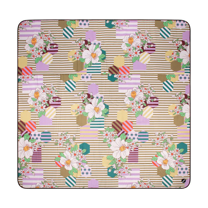 A square picnic mat featuring a detailed patchwork pattern with floral bouquets, striped panels, and geometric shapes in pastel colors on a beige background.