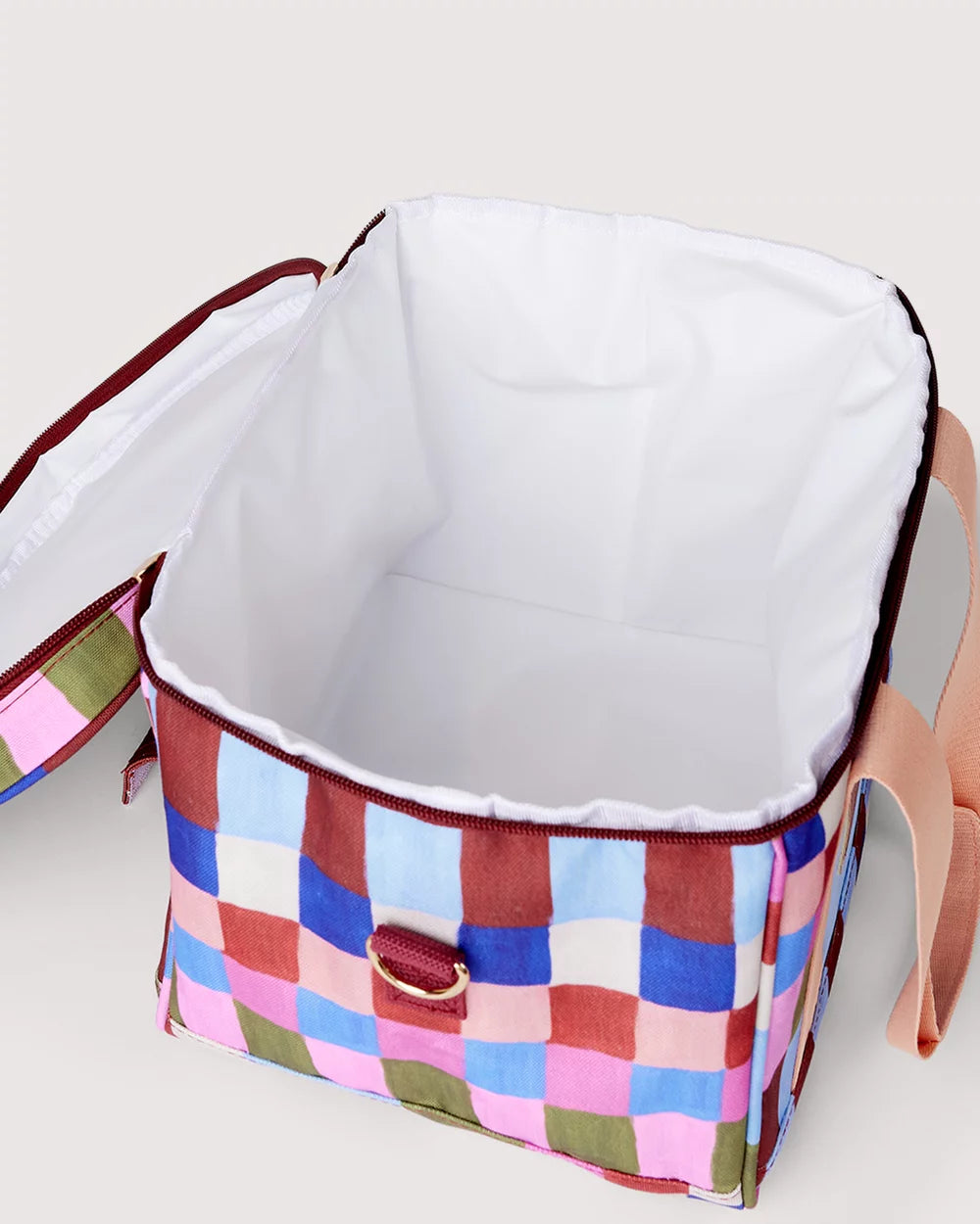 A square soft-sided cooler bag with a colorful patchwork checkered exterior and a white insulated interior, shown open on a light beige background.