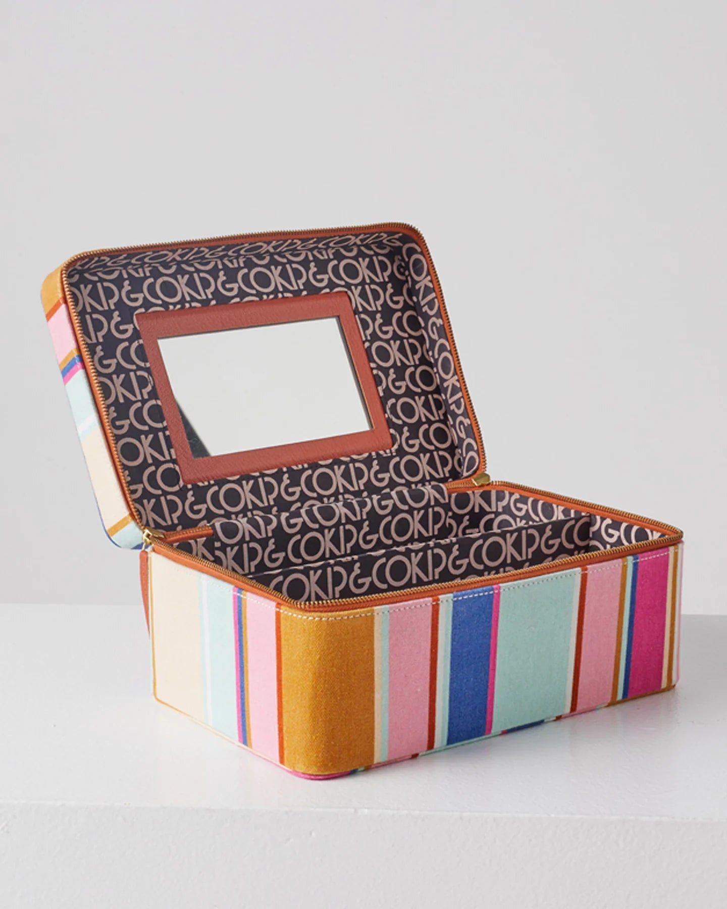 Toiletry case sits open showing mirror on inside of lid, kip and co text is the fabric for inner lining and a single divider in base of case. Stripe pattern fabric outer.
