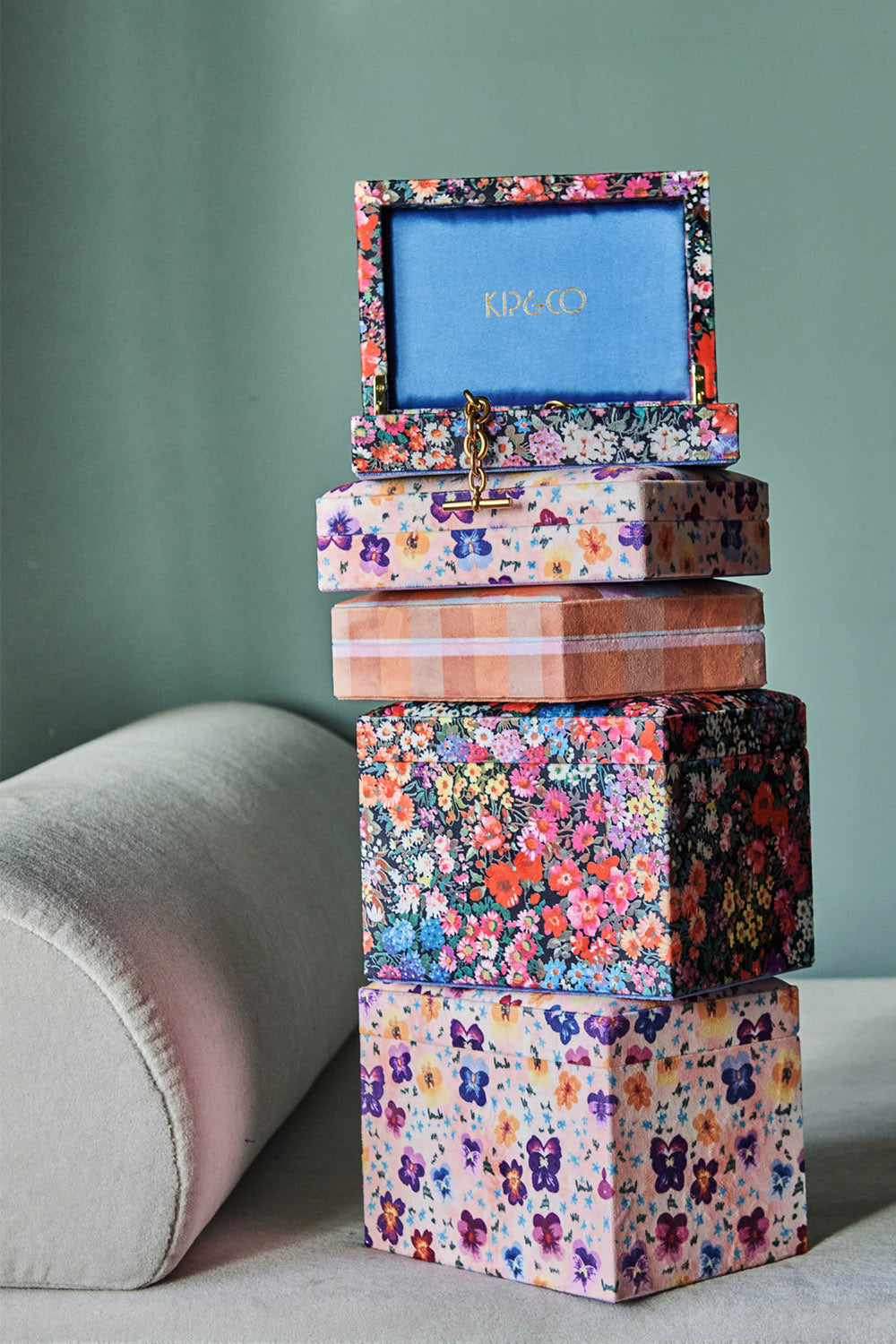 Five velvet jewellery boxes in various sizes stacked on top of one another. Two sizes, various floral and plaid prints.
