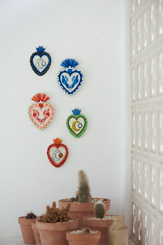 Assorted decorative heart-shaped wall art on a white wall with potted plants on floor.