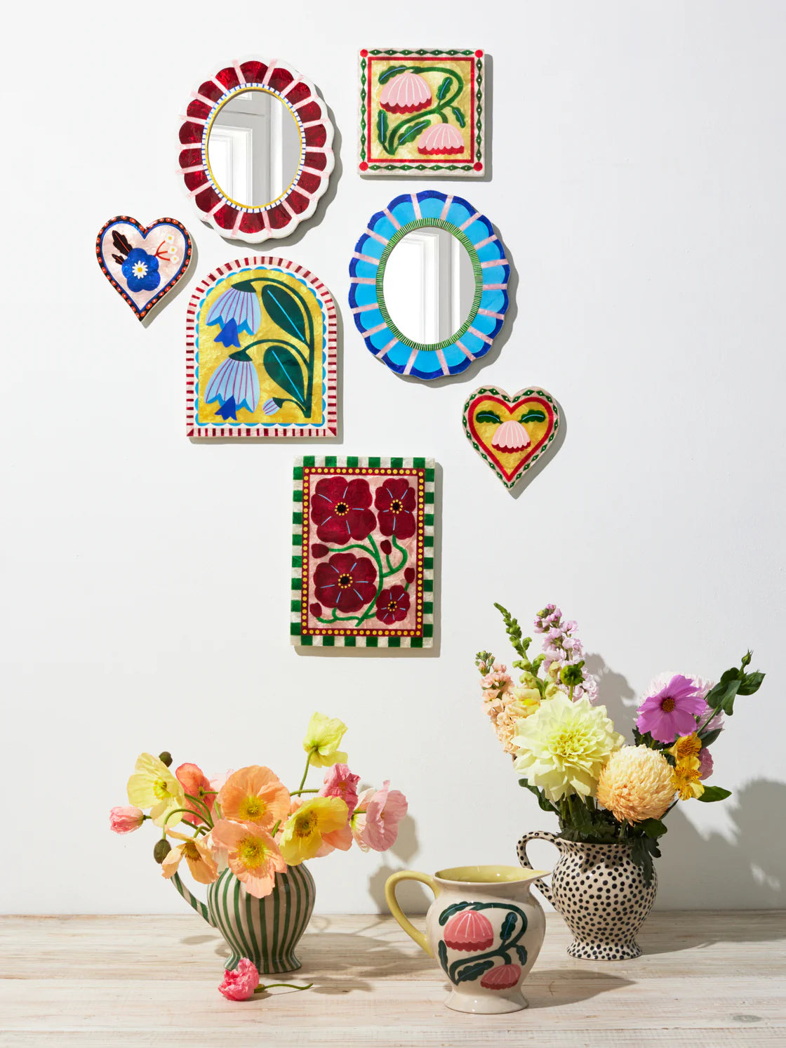 Decorative wall art pieces with floral and abstract designs, accompanied by vases and flowers on a white background.