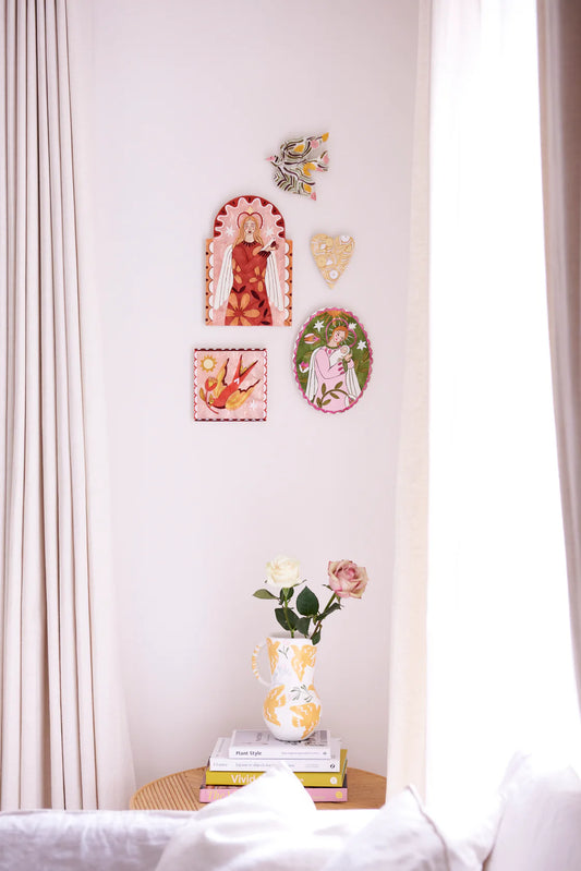 Decorative wall art on a white wall with a vase and books on a table below.