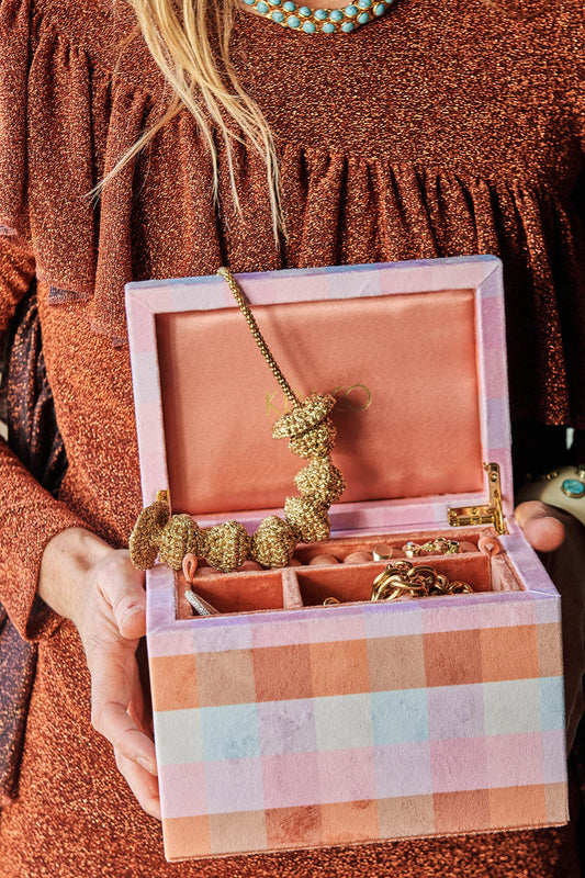 Woman holds velvet jewellery box with gold jewellery inside.