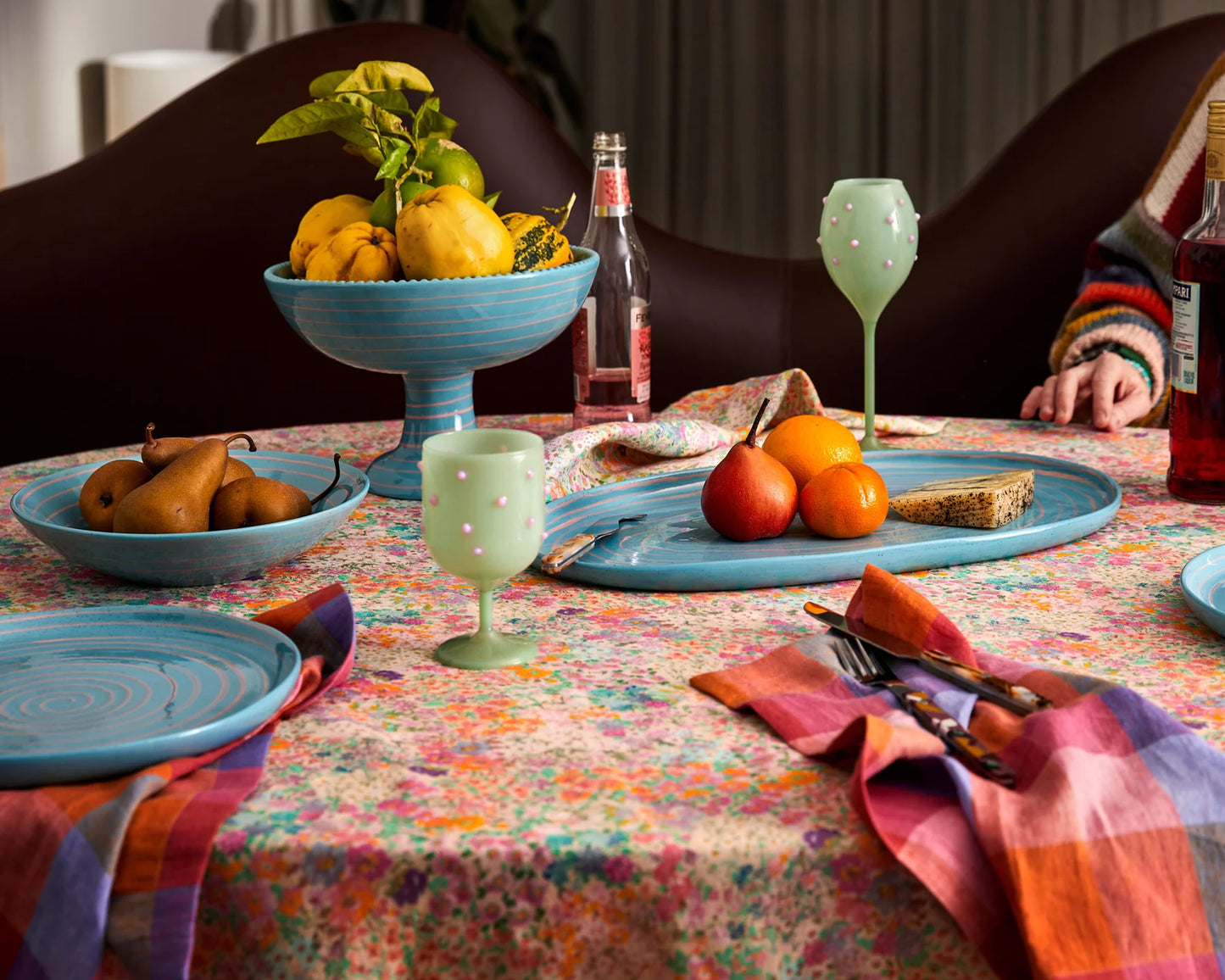 Tablescape with various blue ceramic platters, bowls and plates sat on top of floral tablecloth and rainbow tutti frutti tartan napkins.