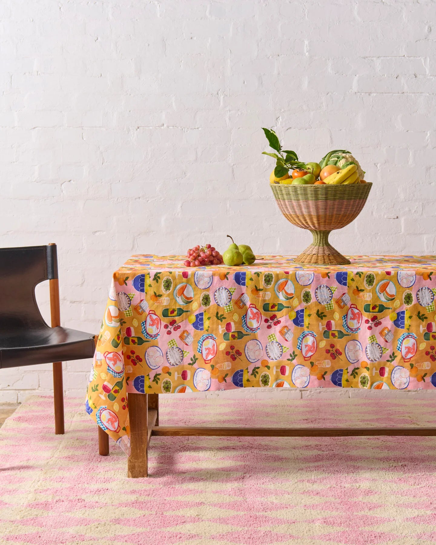 Supper tablecloth laid out on timber table with wicker fruit basket sat on top of table, underneath table is pink and cream geometric rug.
