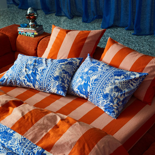 Orange and blue patterned pillows on a bed with a decorative background.