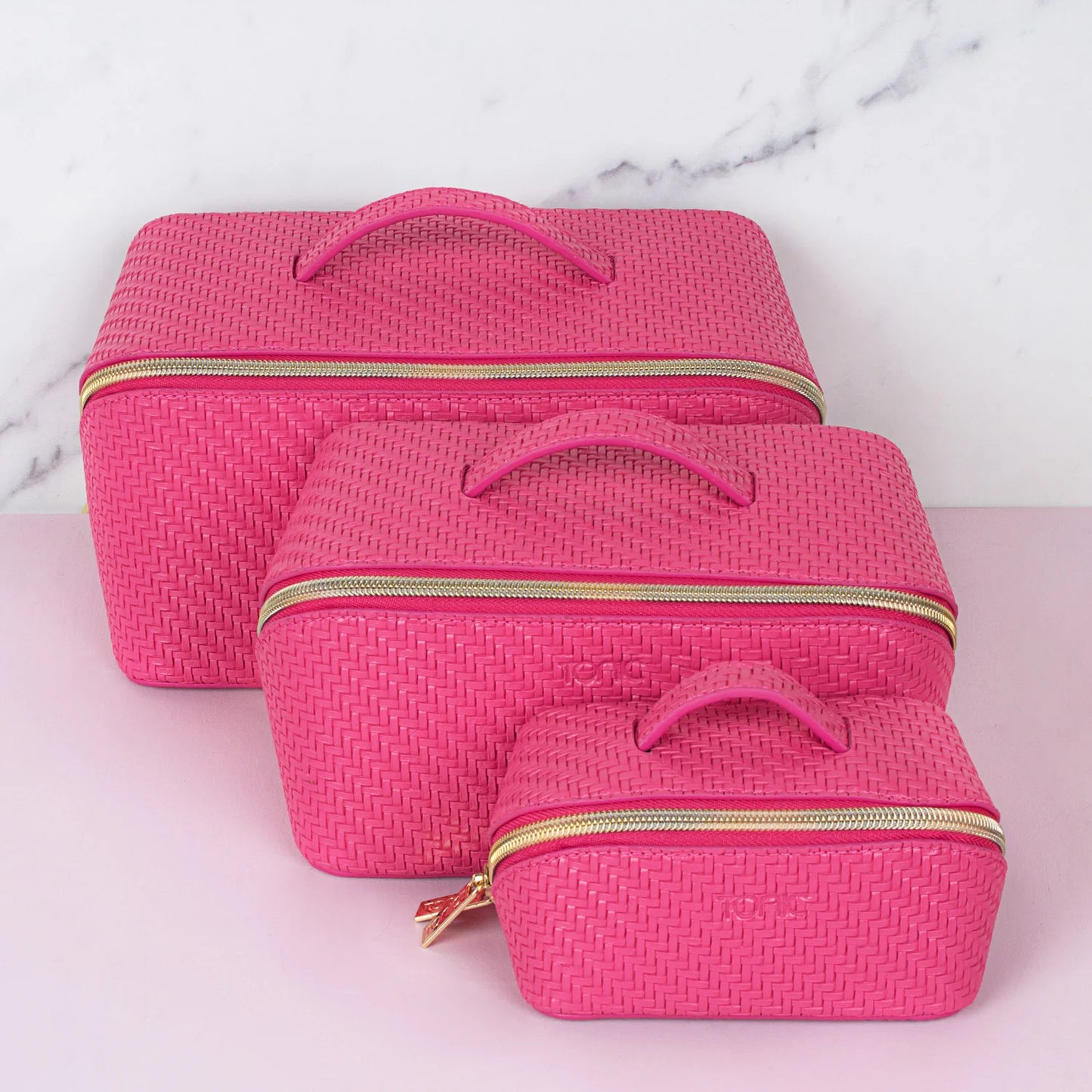 Three pink textured makeup bags in various sizes with gold zippers on a light pink background