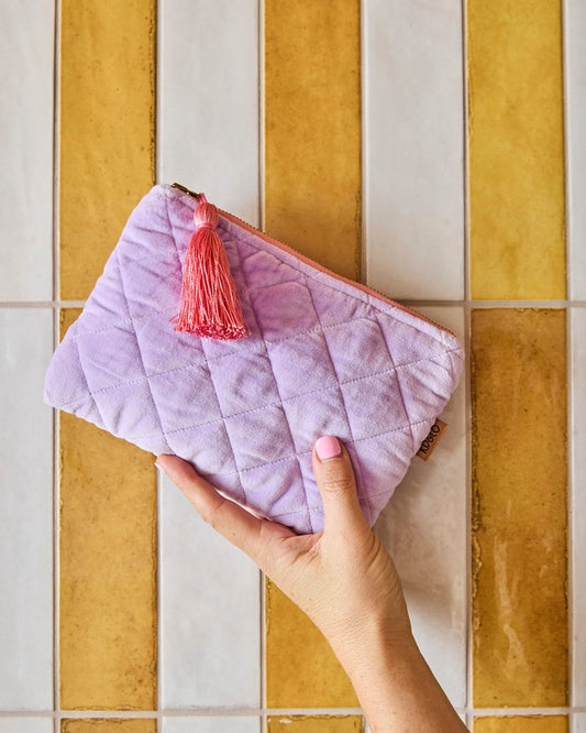 Hand holding a purple quilted pouch with a pink tassel against a tiled wall background