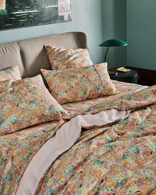 Floral bedding set on a bed with a lamp and painting in the background.
