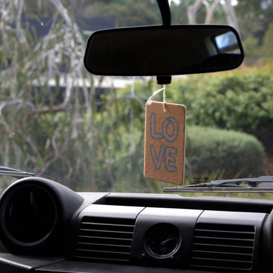 Car interior with a 'LOVE' air freshener hanging from the rearview mirror.