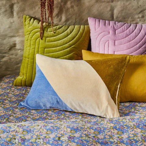 Cornflower blue bedding with assorted green, lilac and mustard cushions.