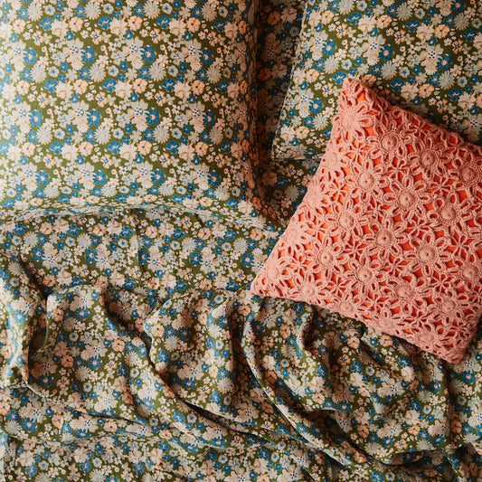 Floral quilt cover, green base, peach, white, grey and blue flower detail. Matching fitted sheet and pillowcases on bed. Along with crochet pink and orange cushion.