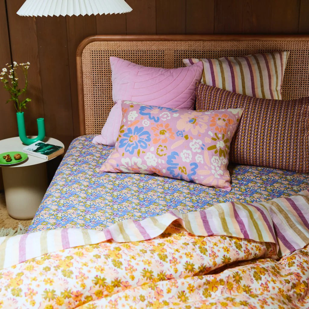 Cream base quilt cover with orange, pink, yellow, and green floral details. Matching floral fitted sheet with blue base, stripe bed sheet and assorted colourful cushions.